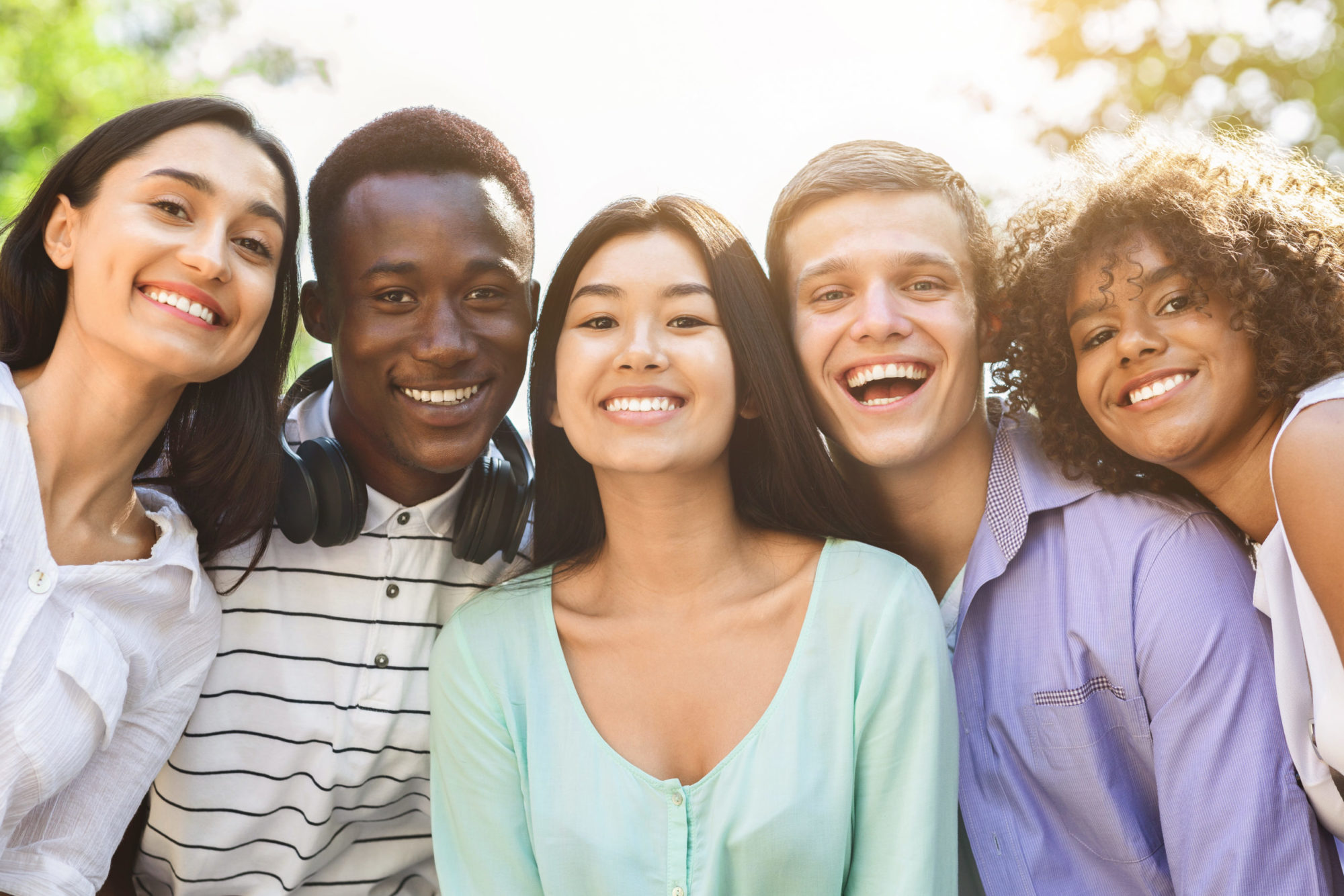 Portrait of cheerful interracial teen friends posing at camera outdoors, smiling and laughing, enjoying spending time together, closeup